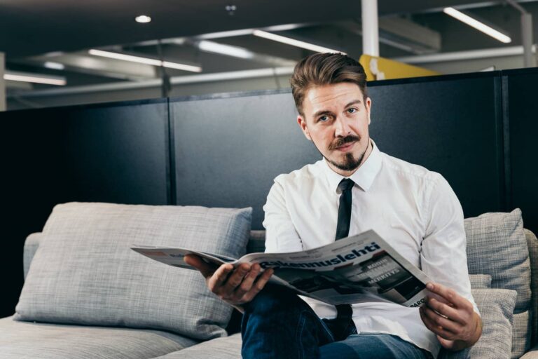 Yrityksen toimitusjohtaja istuu sohvalla ja lukee sanomalehteä
