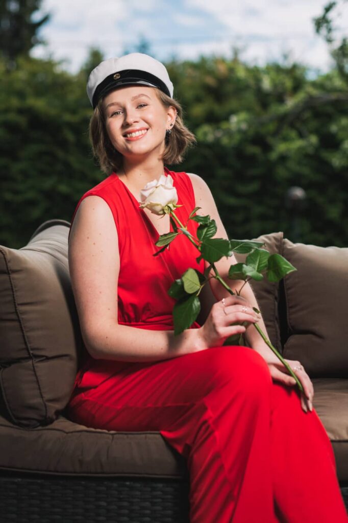 Ylioppilaaksi valmistunut nuori nainen istuu sohvalla ruusu kädessään